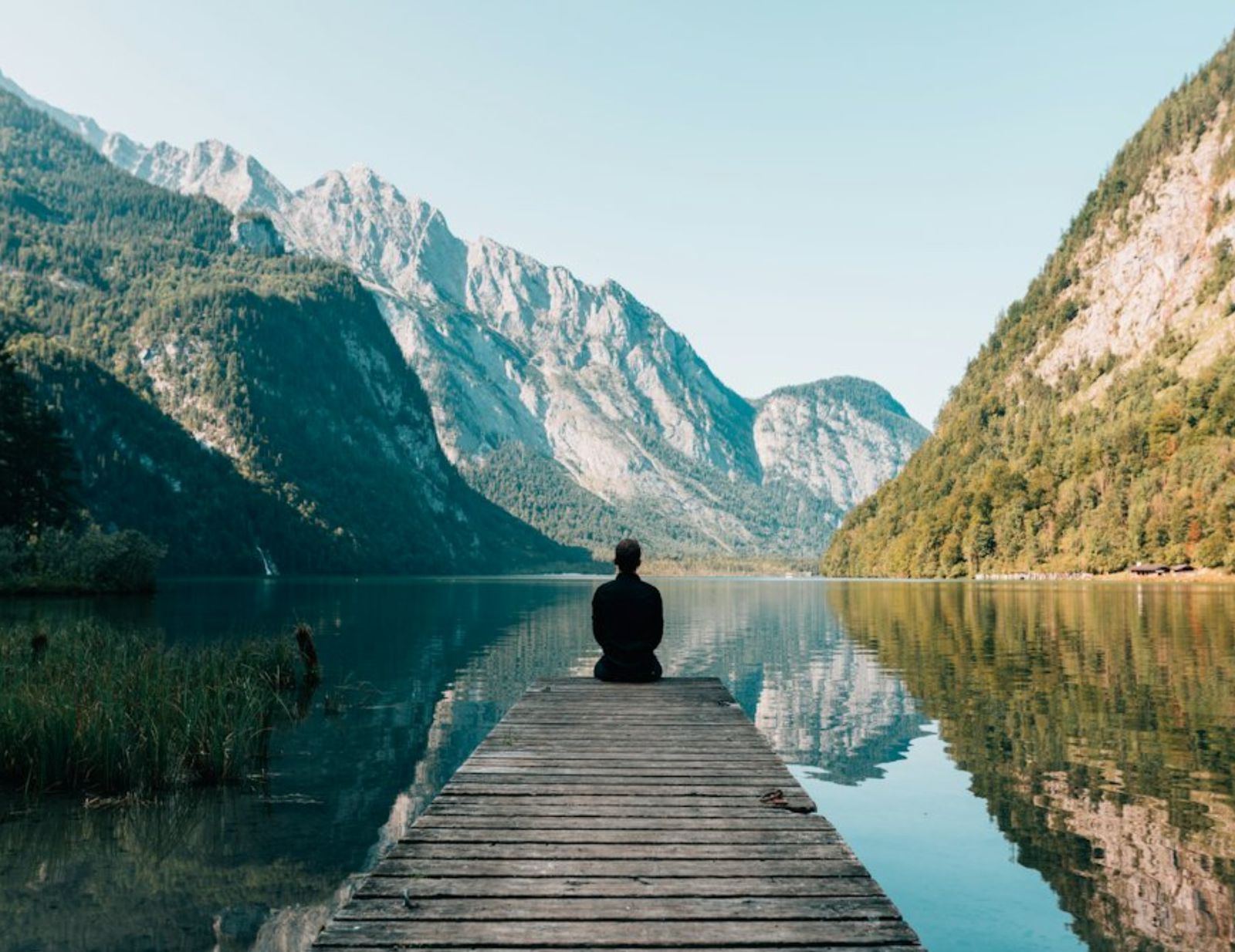 A man sitting at the end of a dock on a mountain lake